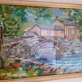 A tapestry picture of the English countryside scene with a stone bridge near a river. 